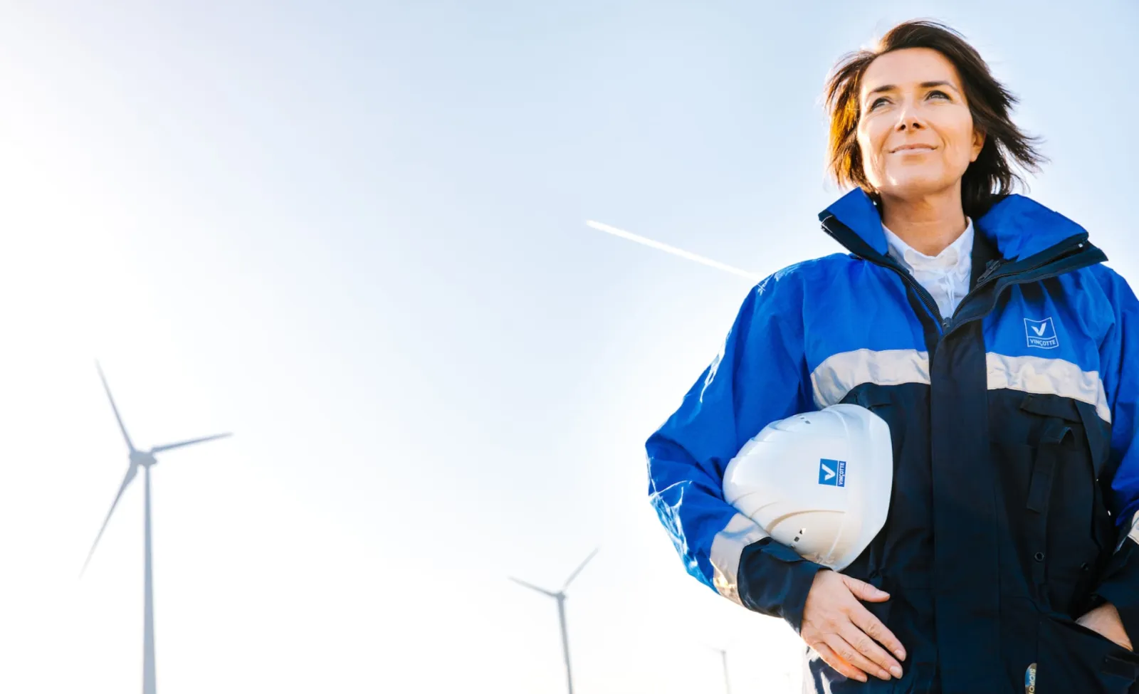 Vinçotte inspector holding a hard hat in front of wind turbines